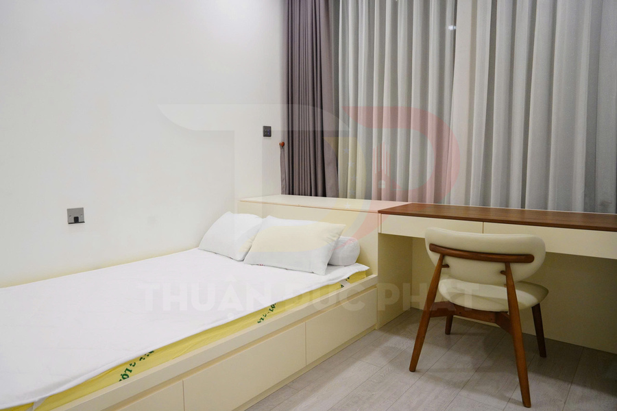 Phòng ngủ nhỏ với giường đơn và bàn làm việc gỗ màu kem cạnh cửa sổ rèm xám