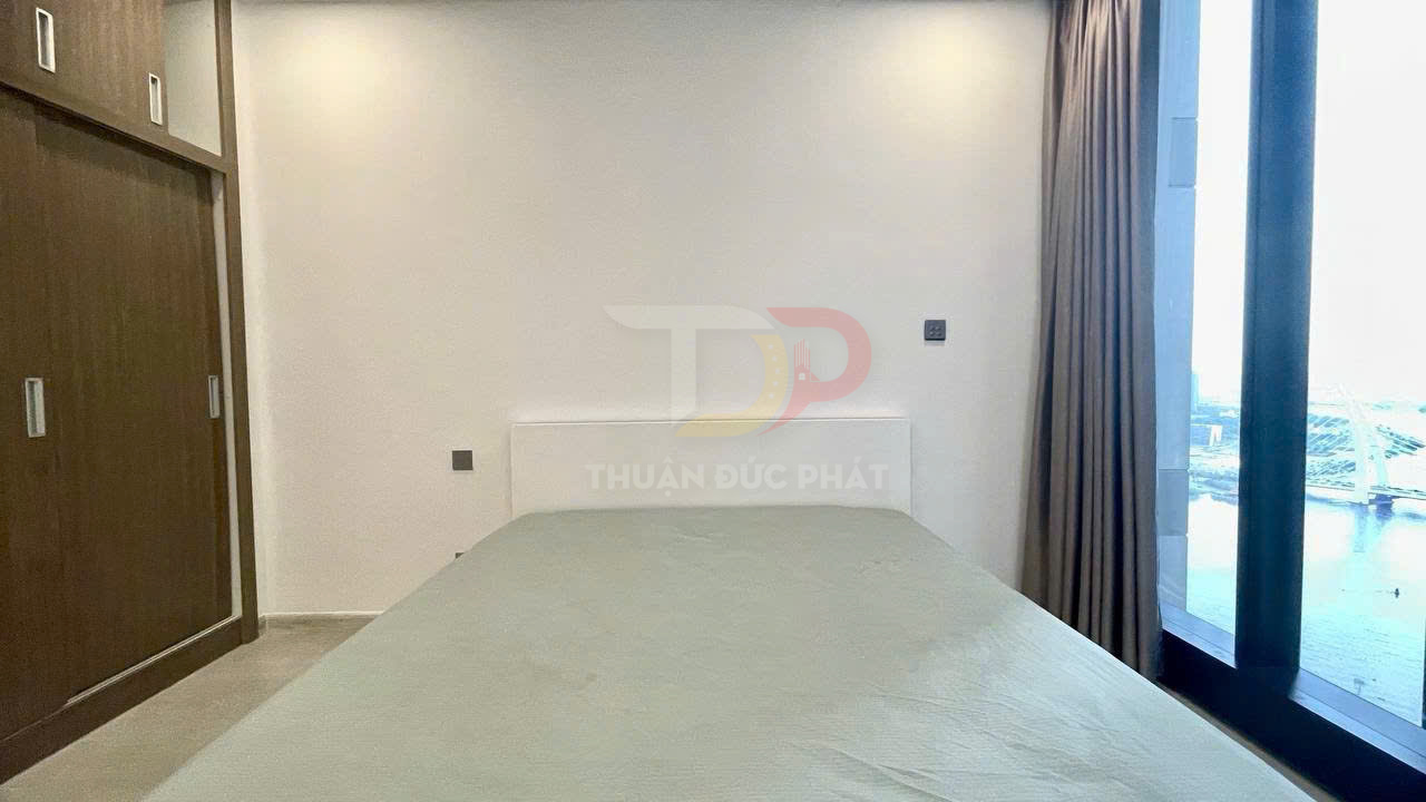 Phòng ngủ tối giản với giường đôi ga xanh nhạt, tủ quần áo gỗ và cửa sổ lớn nhìn ra cảnh thành phố