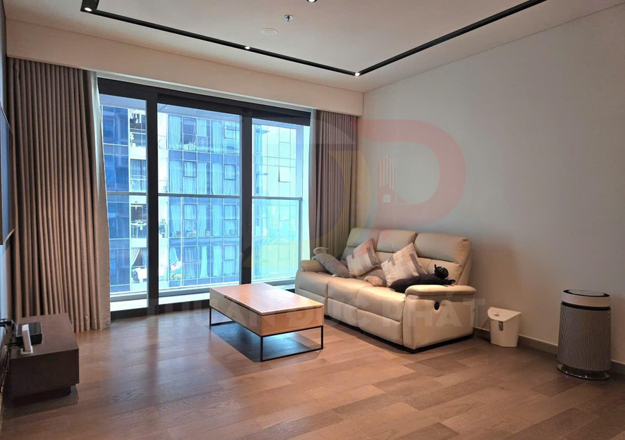 Phòng khách chung cư hiện đại với sofa da màu kem, bàn trà gỗ và cửa kính lớn nhìn ra tòa nhà bên ngoài