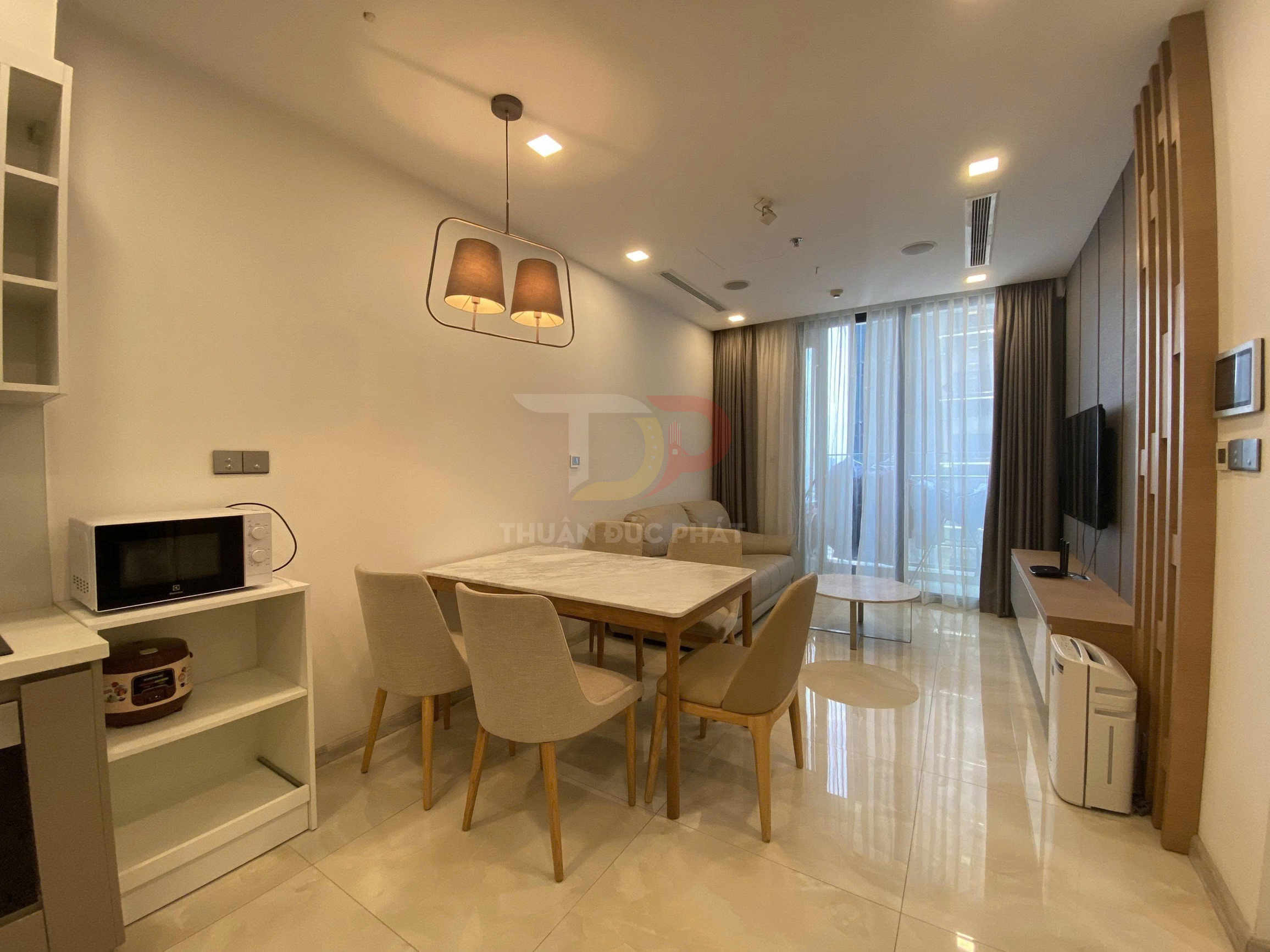 Phòng khách căn hộ hiện đại với bộ bàn ăn gỗ, sofa sáng màu, tivi treo tường và cửa kính lớn có rèm.
