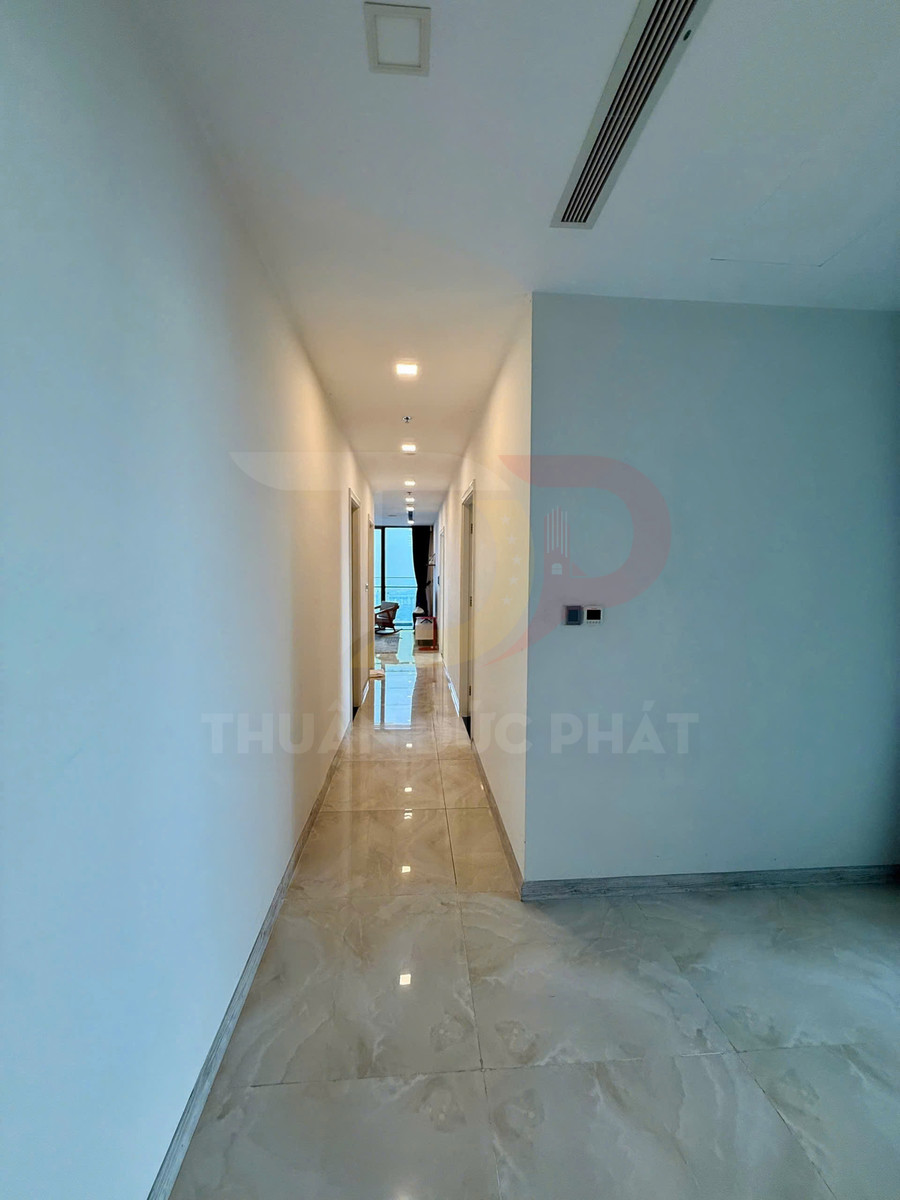 Hành lang căn hộ lát gạch bóng, tường trắng, trần đèn âm trần dẫn ra phòng khách có cửa kính lớn