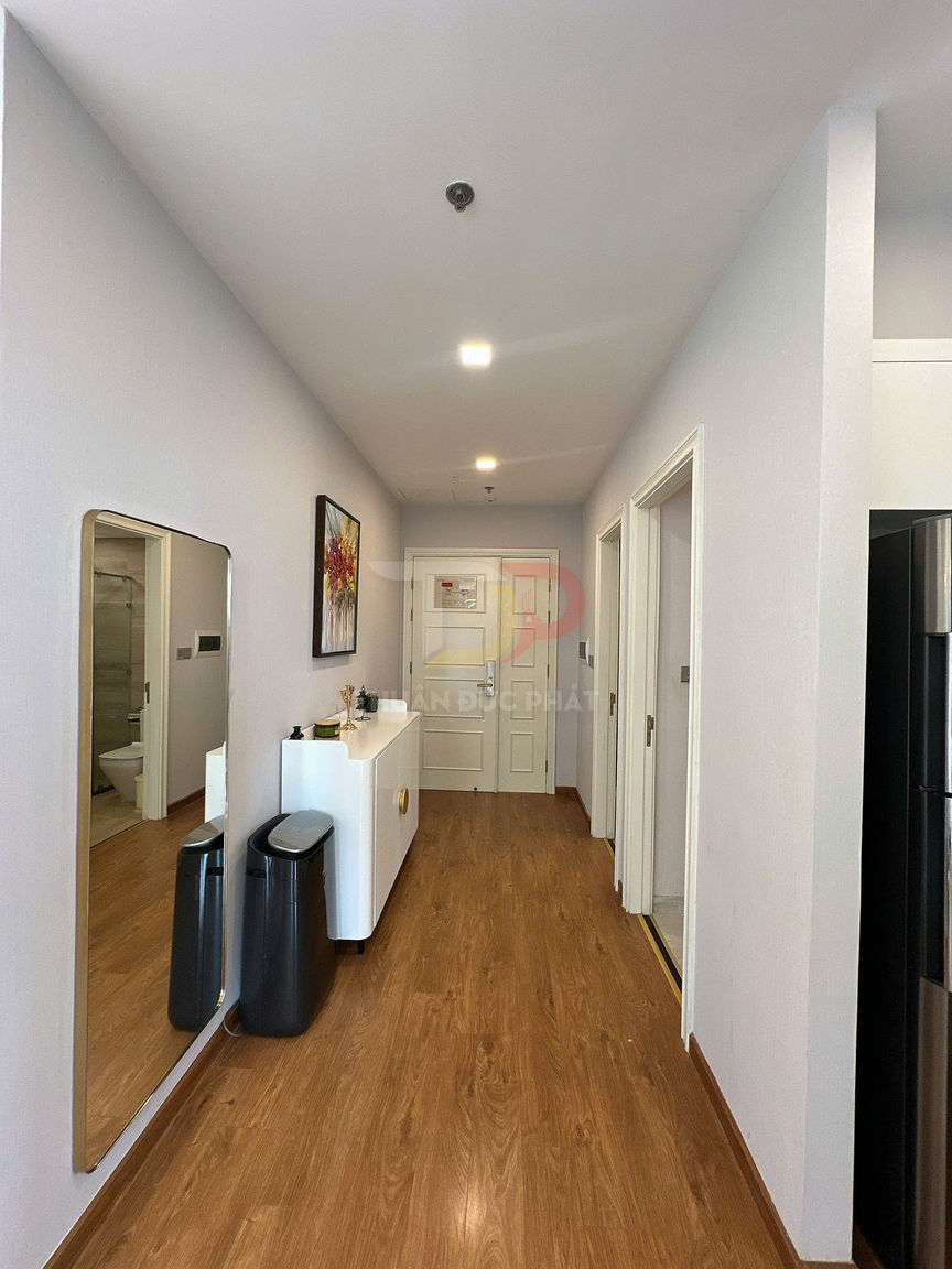 Hành lang căn hộ lát sàn gỗ với tủ giày trắng, gương toàn thân và thùng rác hiện đại