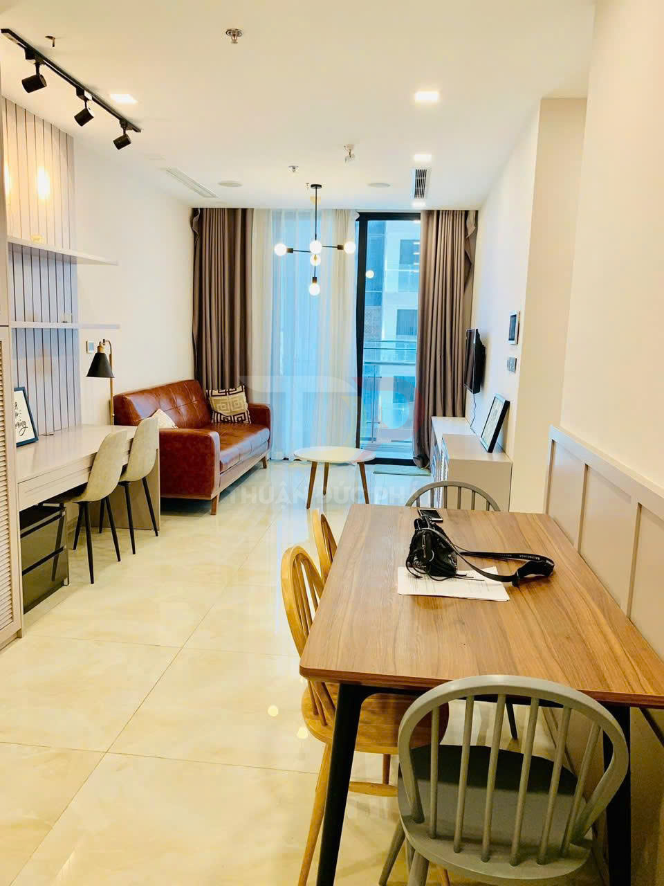 Phòng khách căn hộ hiện đại với bàn ăn gỗ, sofa da nâu và cửa kính lớn đón ánh sáng tự nhiên