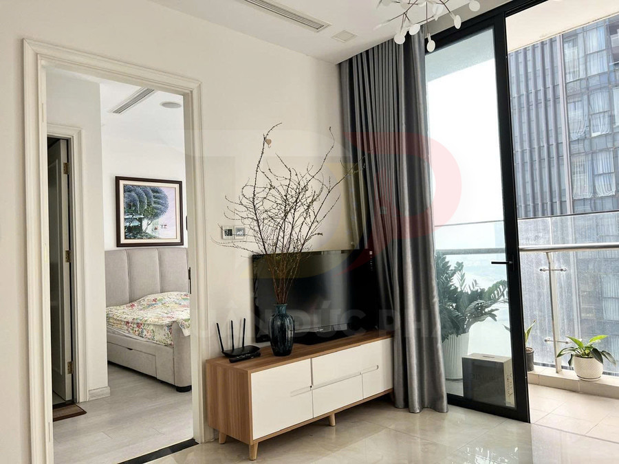 Kệ tivi gỗ hiện đại đặt cạnh cửa kính ban công, trang trí bình hoa và cây xanh trong căn hộ sáng sủa