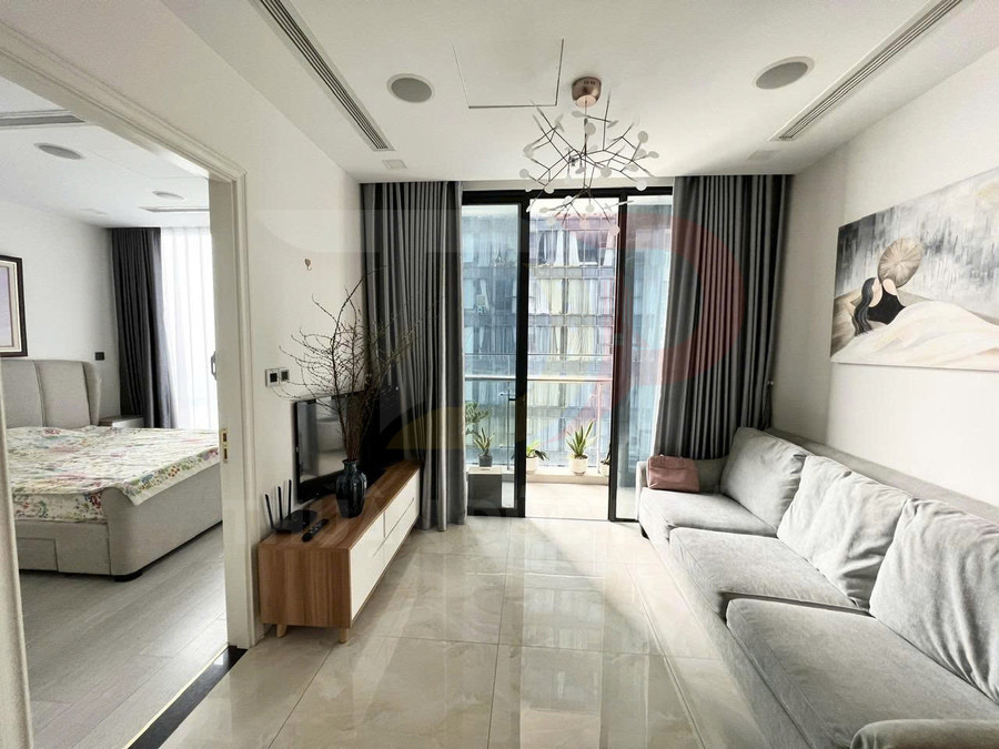 Phòng khách căn hộ hiện đại với sofa xám, kệ tivi gỗ và cửa kính lớn nhìn ra ban công có cây xanh
