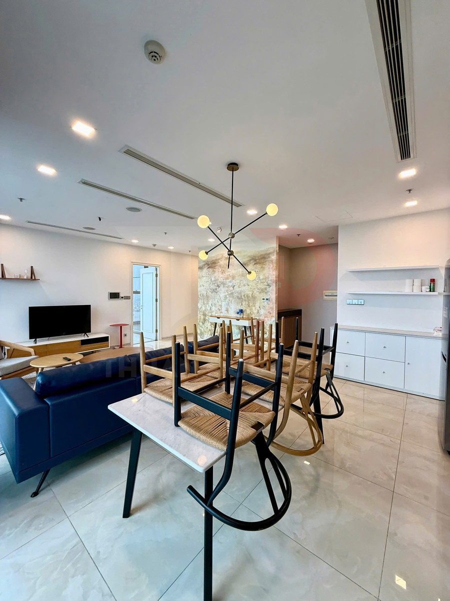 Bàn ăn mặt đá với ghế gỗ lật úp trong phòng khách hiện đại có sofa da xanh và tivi màn hình phẳng