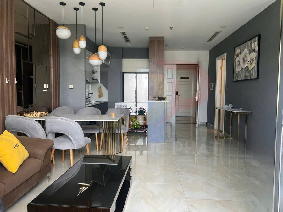 Phòng khách căn hộ hiện đại với sofa nâu, bàn trà kính đen và bộ bàn ăn ghế bọc nỉ xám cạnh bếp mở