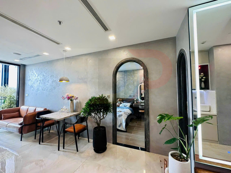 Phòng khách căn hộ hiện đại với sofa da, bàn ăn nhỏ cạnh cửa vòm dẫn vào phòng ngủ