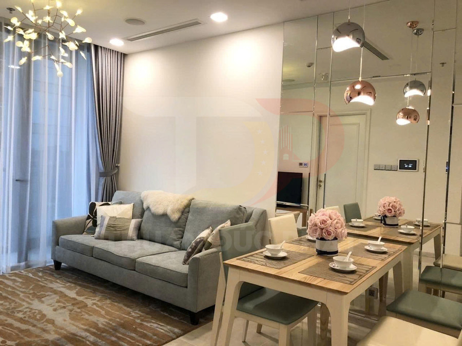 Phòng khách căn hộ hiện đại với sofa xám, bàn ăn gỗ bày bộ bát đĩa và đèn thả trang trí sang trọng