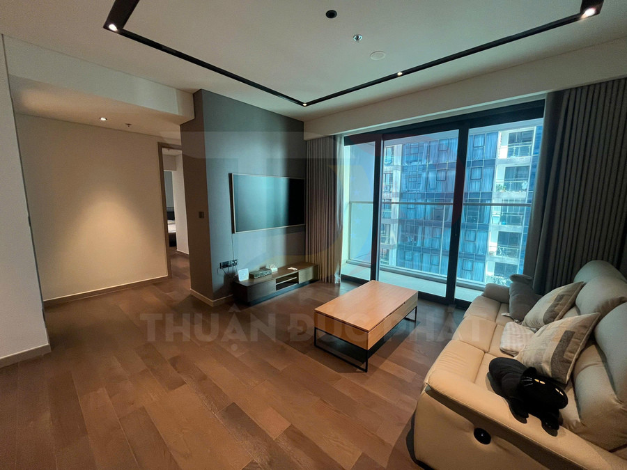 Phòng khách căn hộ hiện đại với sofa da, bàn trà gỗ, tivi treo tường và cửa kính lớn nhìn ra chung cư
