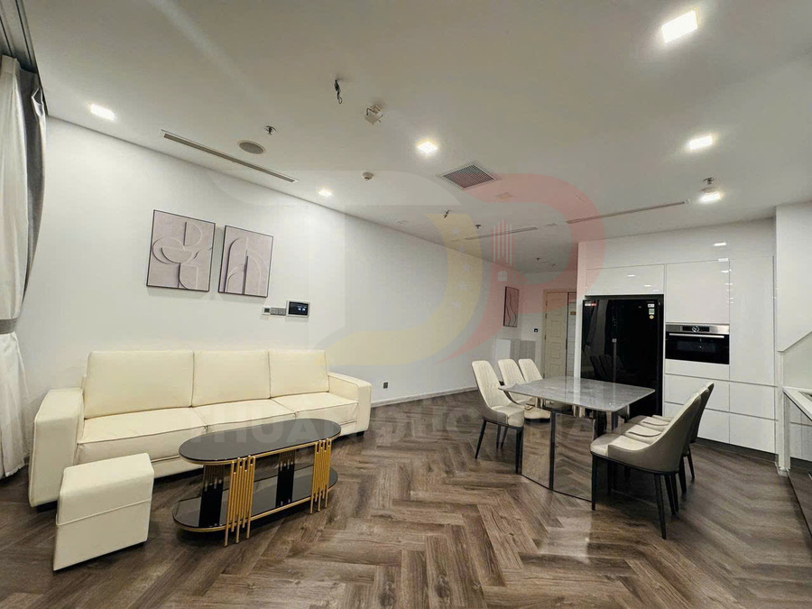 Phòng khách và bếp hiện đại với sofa chữ L màu kem, bàn trà, bàn ăn đá và tủ bếp trắng liền kề tủ lạnh đen