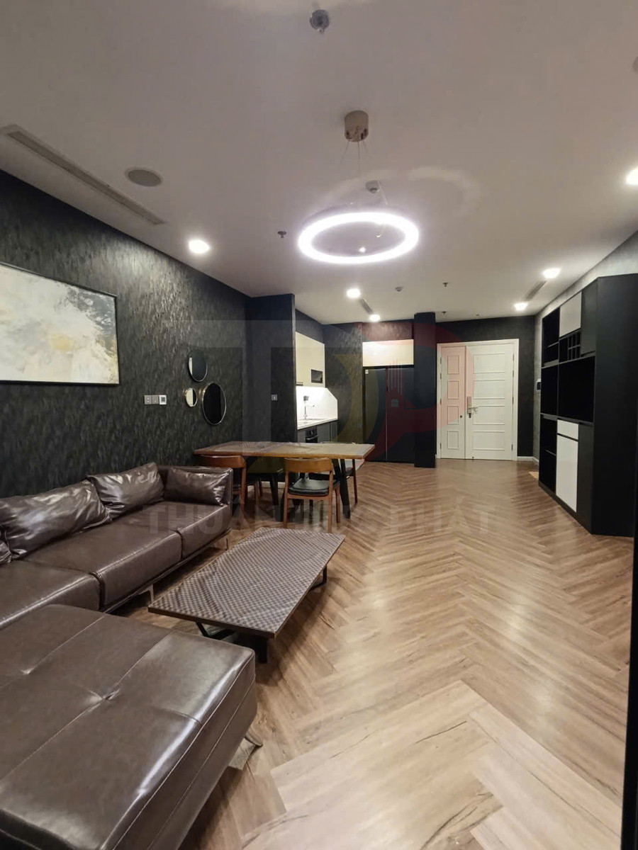 Phòng khách chung cư hiện đại với sofa da nâu, bàn trà gỗ và bếp liền kề sàn gỗ xương cá