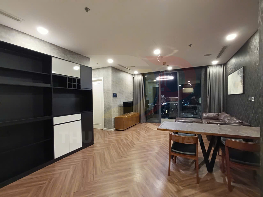 Phòng khách chung cư hiện đại với sàn gỗ, kệ tivi, sofa da và bàn ăn cạnh cửa kính lớn nhìn ra thành phố