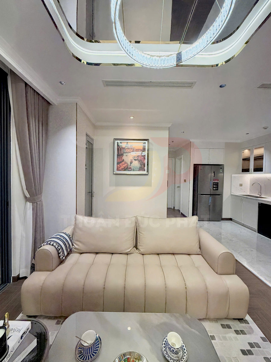 Sofa da màu be hiện đại trong phòng khách chung cư, phía sau là bếp và tủ lạnh inox