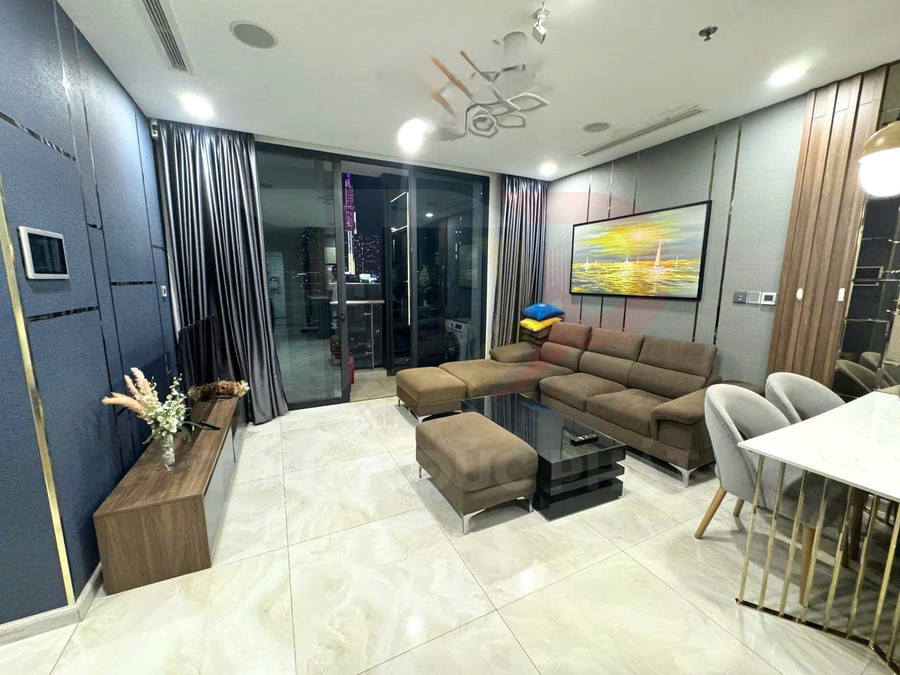 Phòng khách chung cư hiện đại với sofa góc nỉ màu nâu, bàn trà kính đen và cửa kính lớn nhìn ra ban công