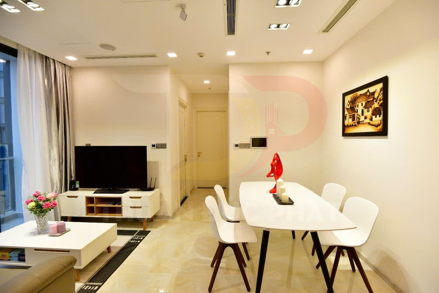 Phòng khách căn hộ hiện đại với bàn ăn trắng bốn ghế, tivi màn phẳng và nội thất tối giản sáng màu