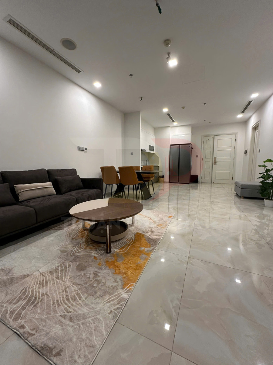 Phòng khách căn hộ hiện đại với sofa xám, bàn trà gỗ tròn và bếp liền kề sáng màu