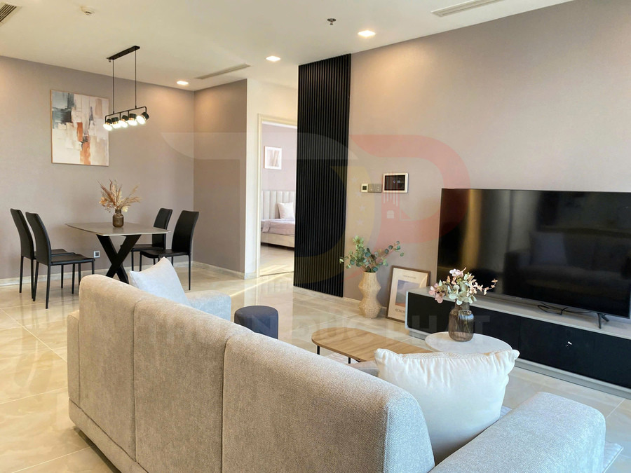 Phòng khách căn hộ hiện đại với sofa vải màu be, bàn trà gỗ và tivi màn hình phẳng cỡ lớn trên kệ thấp
