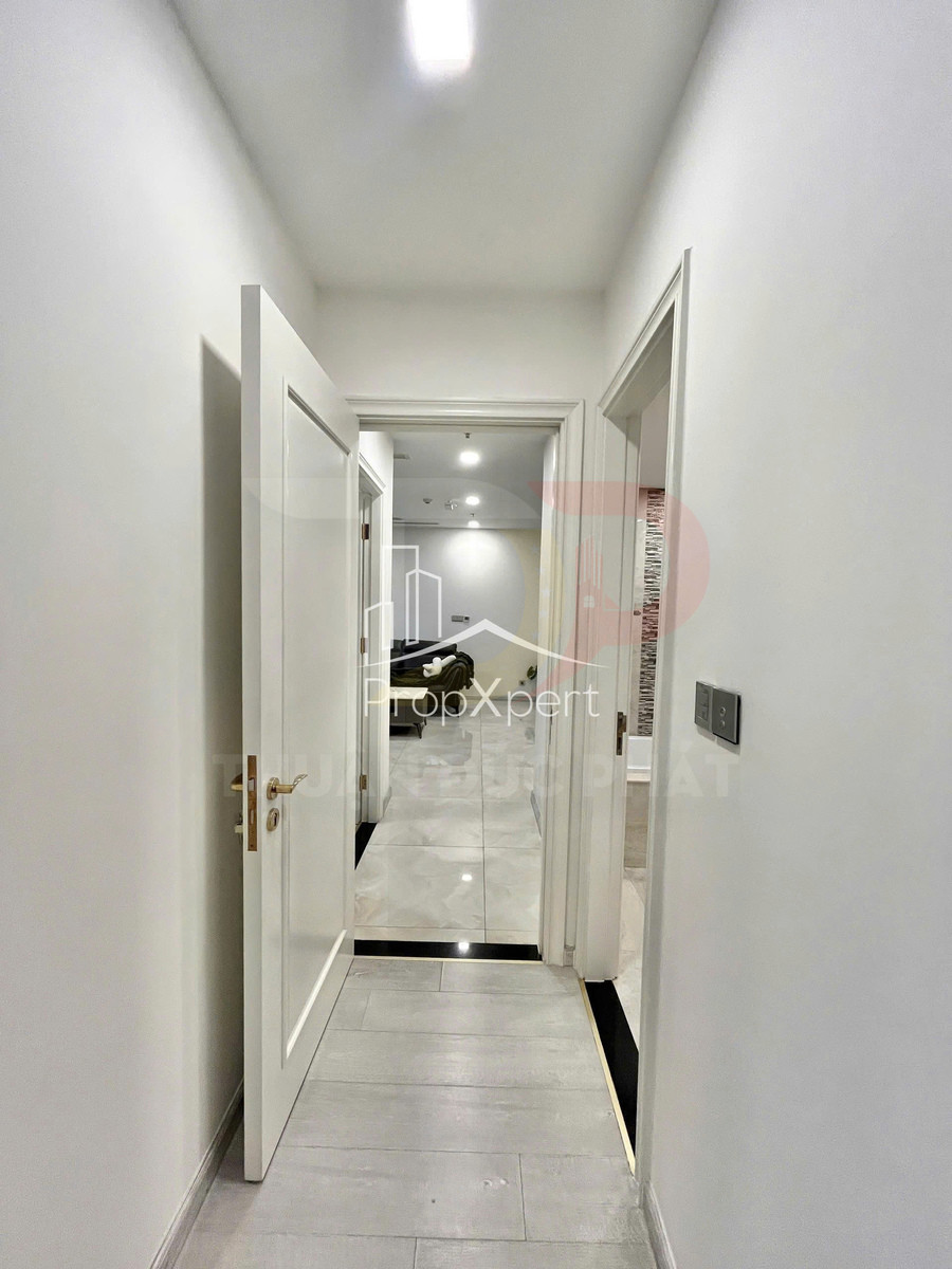 Hành lang căn hộ hiện đại với cửa gỗ trắng mở ra phòng khách lát gạch sáng