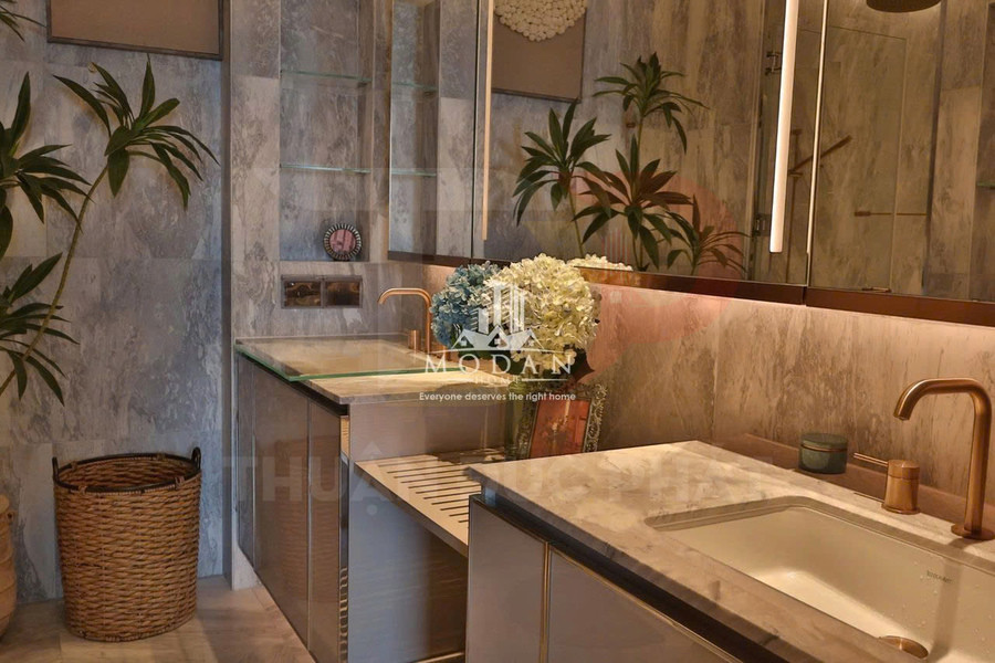 Phòng tắm hiện đại với lavabo đá, vòi nước màu vàng đồng và kệ kính trang trí hoa tươi