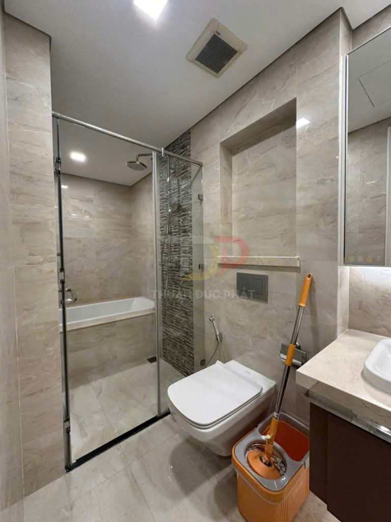 Phòng tắm hiện đại với bồn tắm kính, bồn cầu treo tường và bộ cây lau nhà màu cam