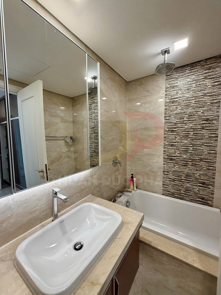 Phòng tắm hiện đại với bồn rửa mặt sứ trắng, vòi nước inox và bồn tắm nằm cạnh tường ốp đá trang trí