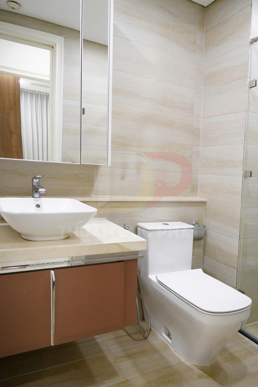 Bồn cầu sứ trắng hiện đại cạnh lavabo đặt trên tủ gỗ trong phòng tắm ốp gạch sáng màu
