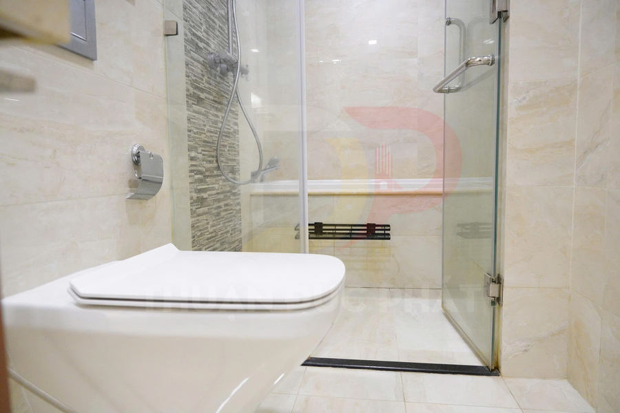 Bồn cầu treo tường hiện đại cạnh buồng tắm kính và vòi sen trong phòng tắm lát gạch sáng