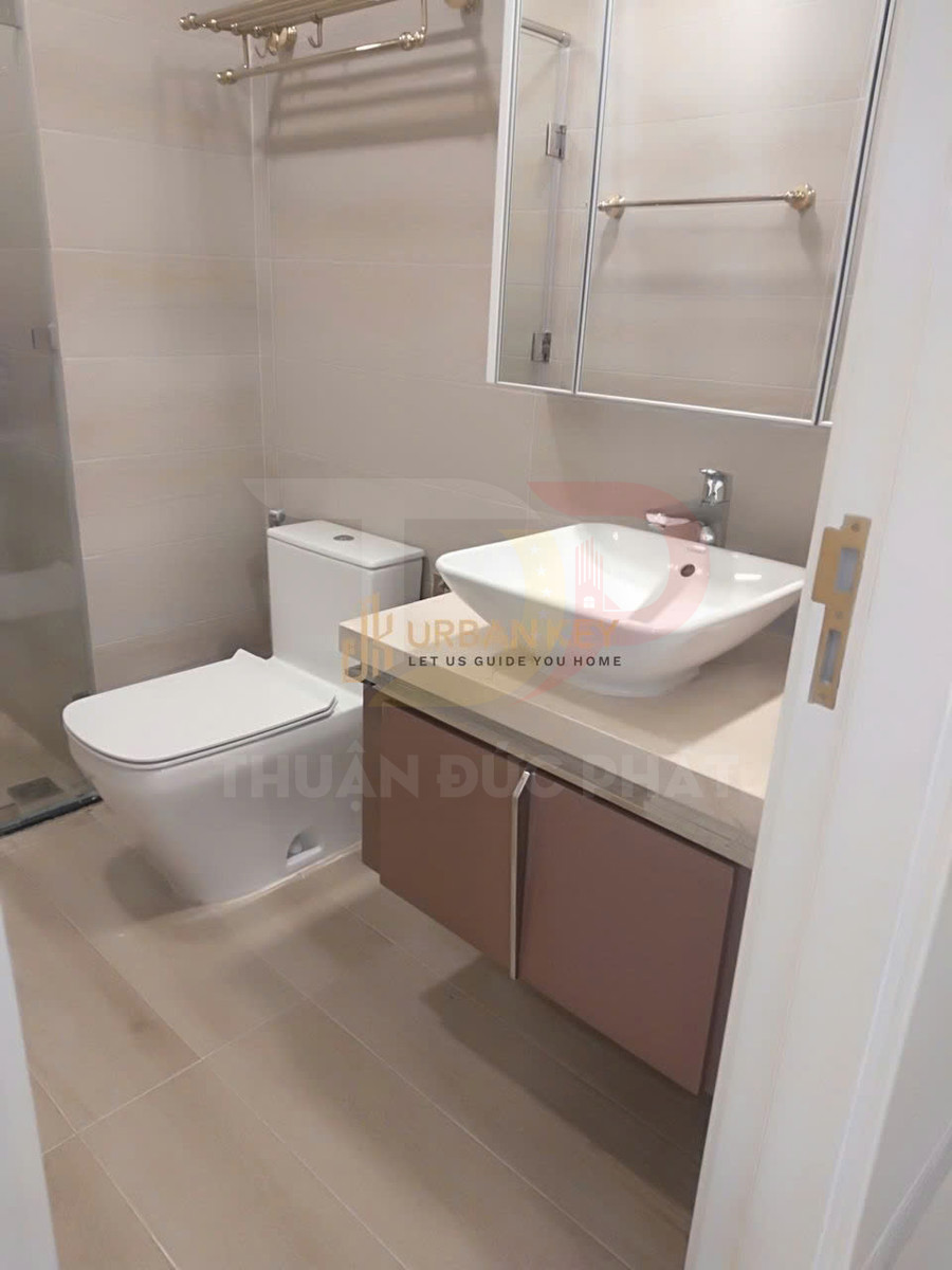 Phòng tắm hiện đại với bồn cầu, lavabo đặt trên tủ gỗ, gương lớn và kệ treo khăn màu vàng đồng
