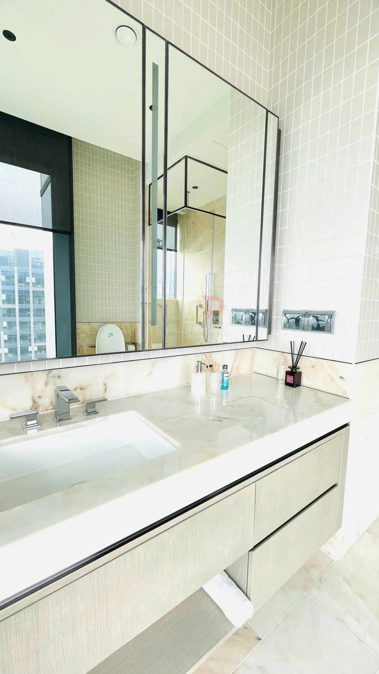 Bồn rửa mặt đá cẩm thạch trong phòng tắm hiện đại với gương lớn và phụ kiện chăm sóc cá nhân