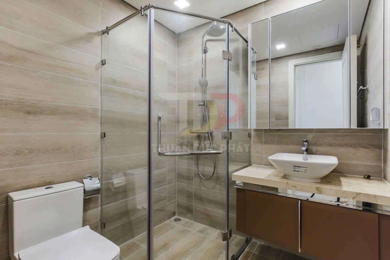 Phòng tắm hiện đại với vách tắm kính cường lực, vòi sen đứng, bồn cầu và lavabo đặt trên mặt đá
