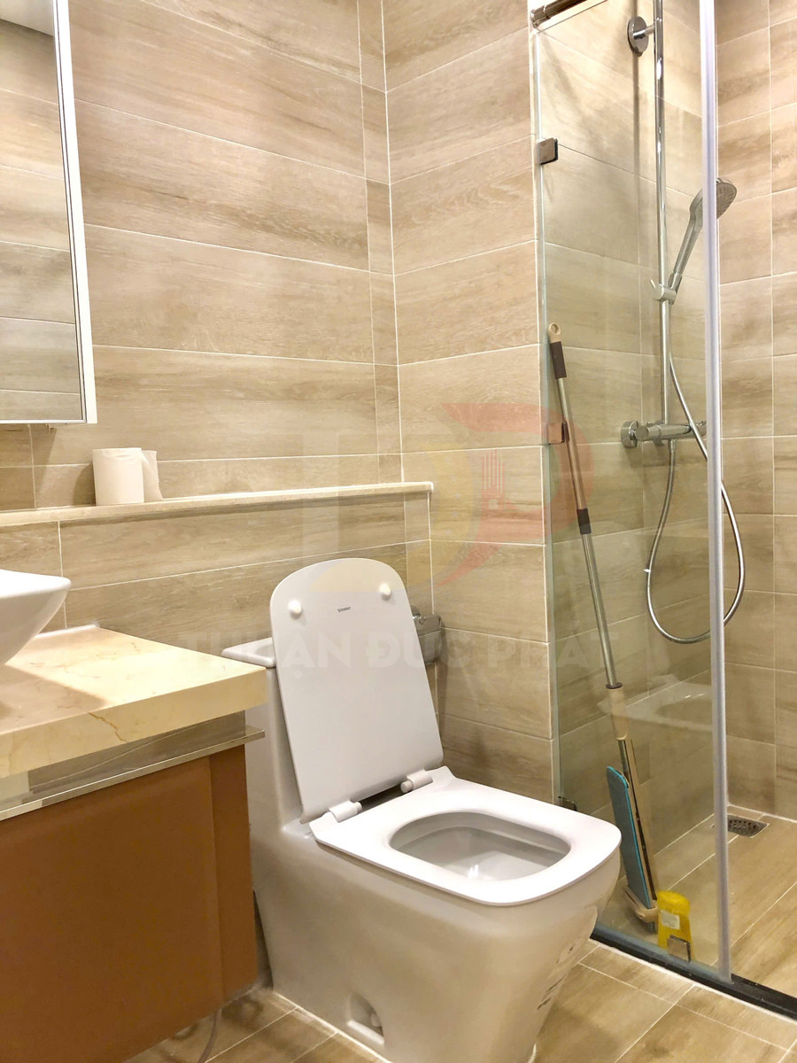 Bồn cầu sứ trắng cạnh buồng tắm kính trong nhà vệ sinh ốp gạch giả gỗ hiện đại