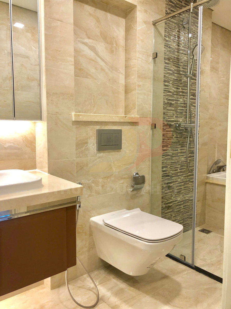 Bồn cầu treo tường hiện đại trong phòng tắm lát đá marble có vách kính tắm đứng