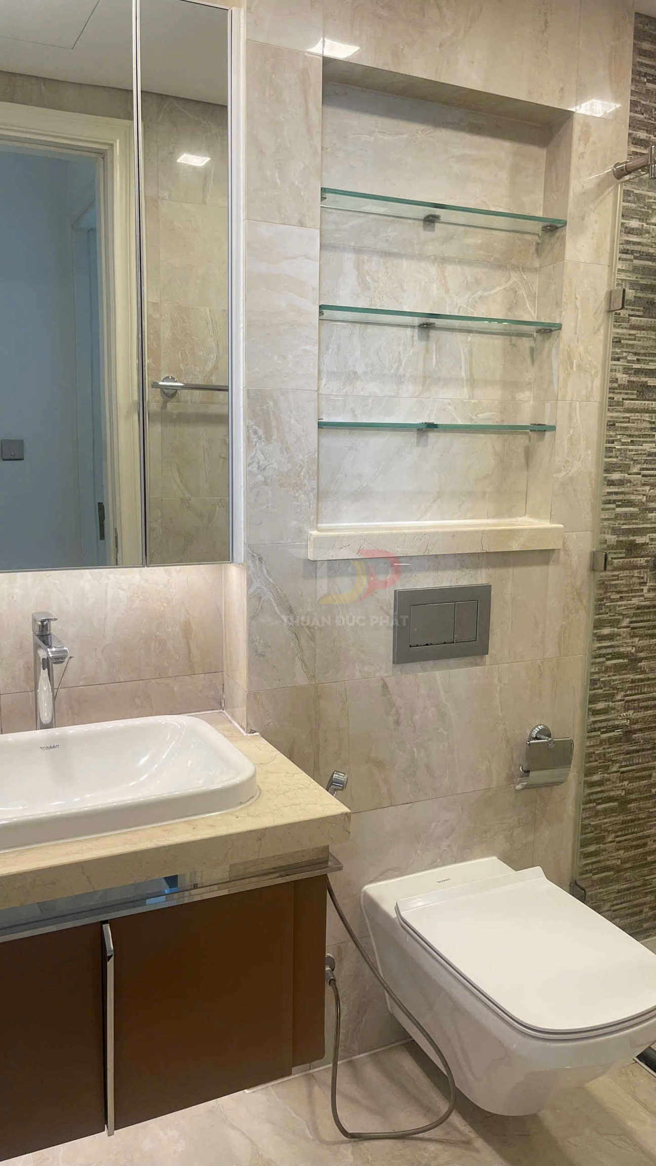 Phòng tắm hiện đại với bồn cầu treo tường, chậu rửa mặt TOTO và kệ kính trên tường đá marble