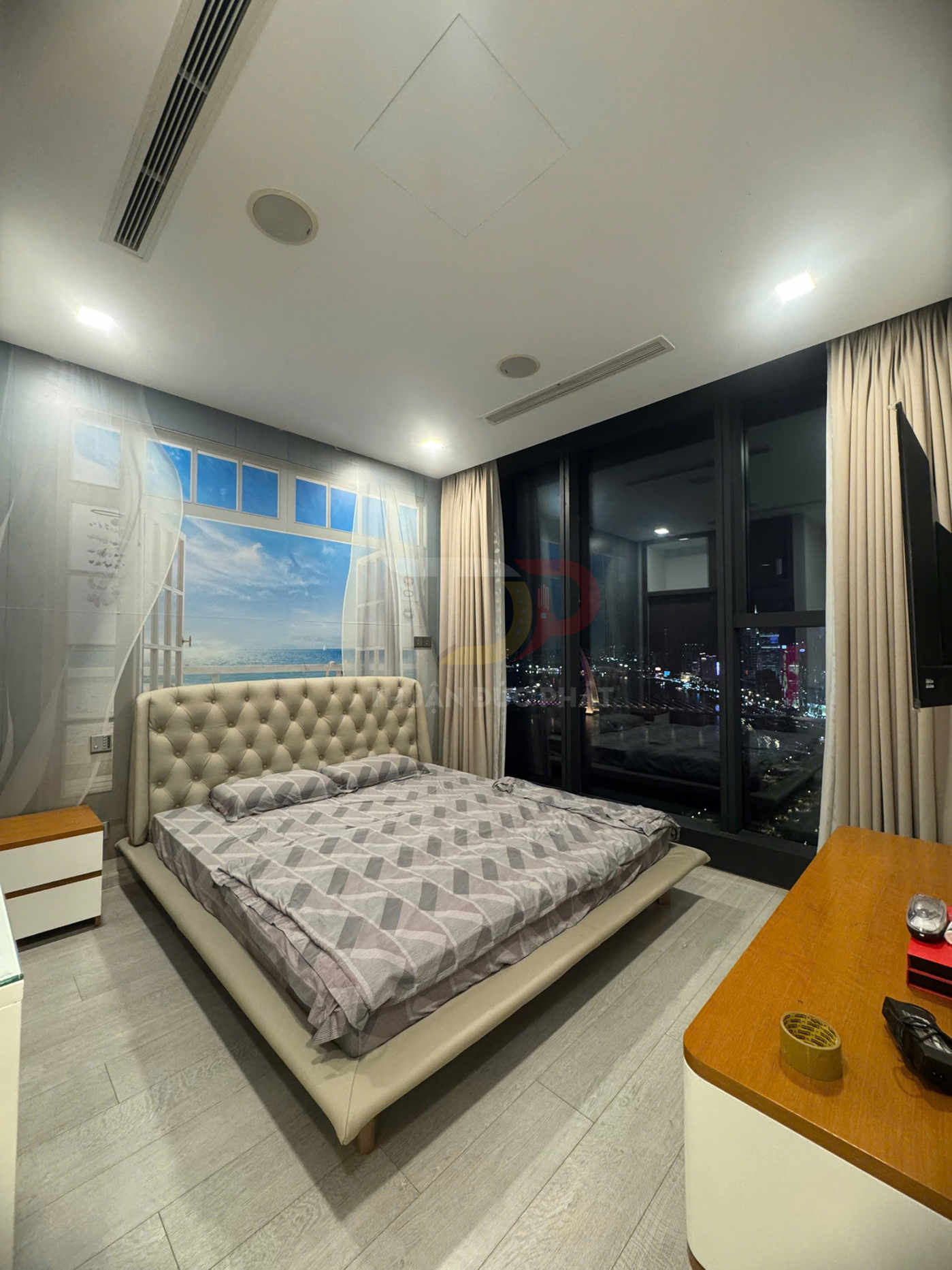 Giường ngủ bọc da màu kem với chăn ga họa tiết hình học trong phòng ngủ hiện đại có cửa kính lớn nhìn ra thành phố