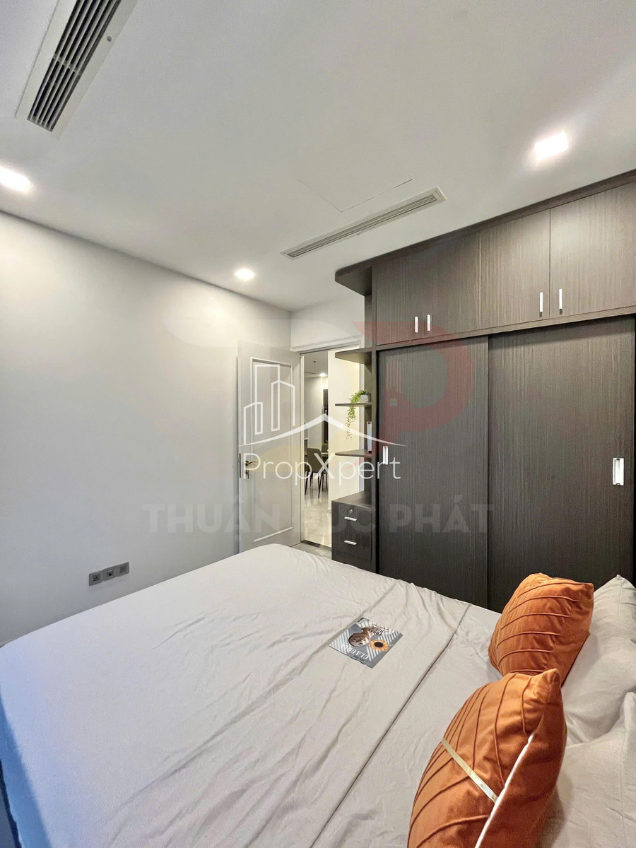 Phòng ngủ hiện đại với giường đôi ga trắng gối cam và tủ quần áo gỗ lớn sát tường