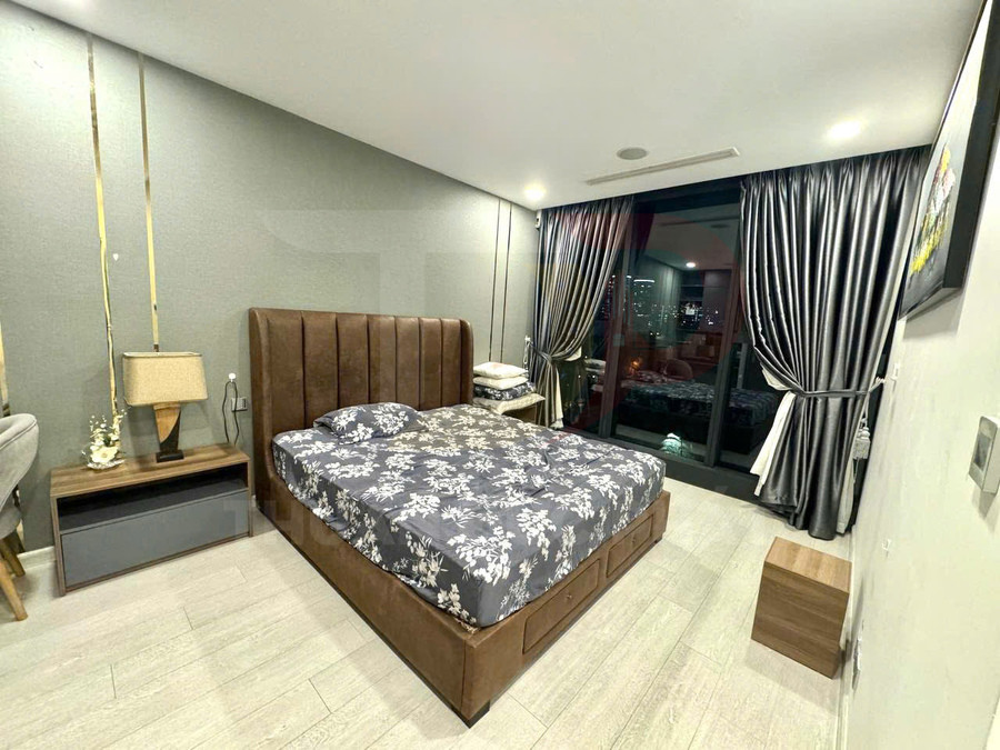 Phòng ngủ hiện đại với giường bọc da nâu, chăn ga hoa tối màu và cửa kính lớn nhìn ra thành phố ban đêm