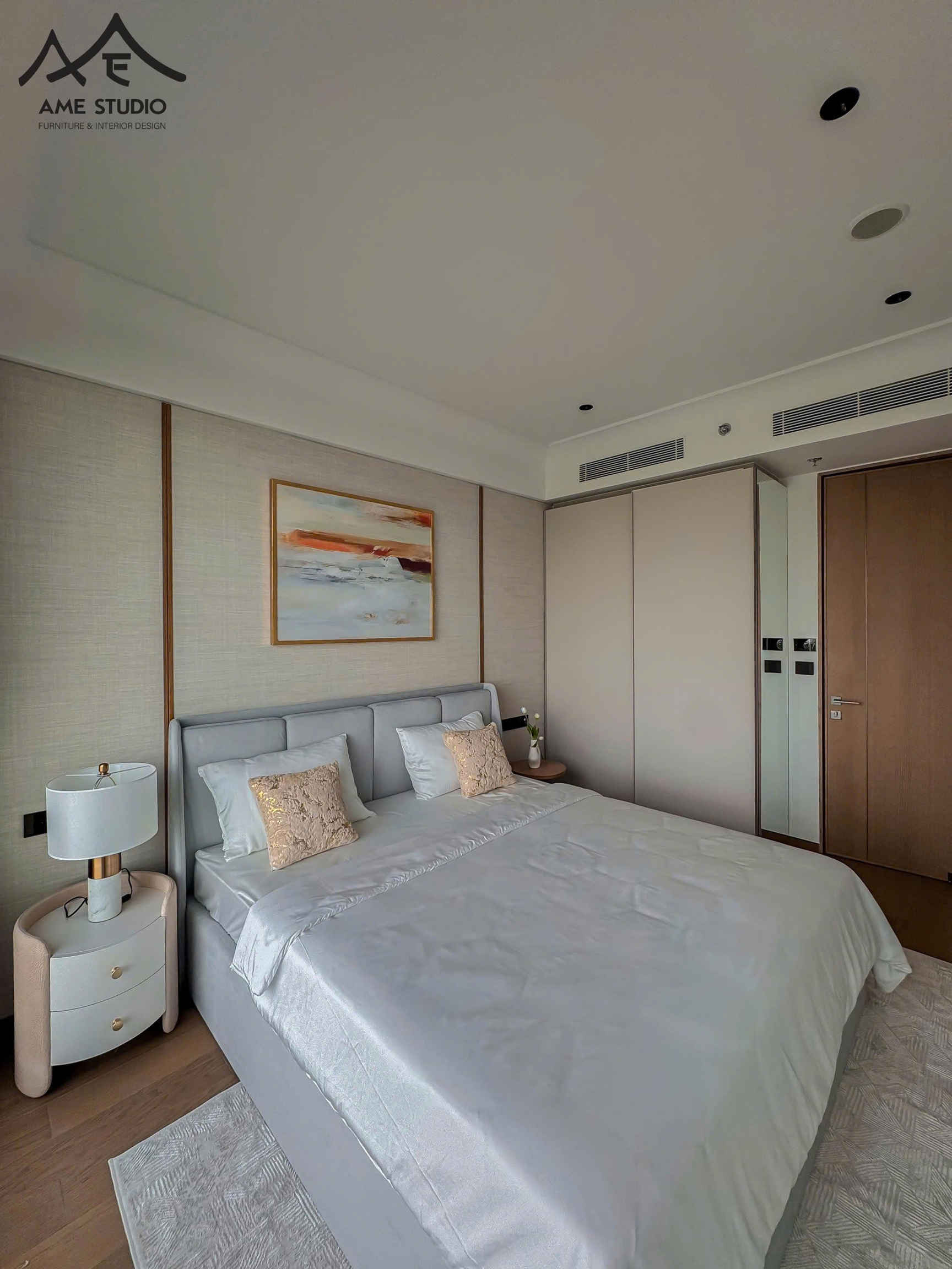 Phòng ngủ hiện đại với giường đôi bọc nệm màu xám, ga gối sáng màu và tủ đầu giường cạnh đèn ngủ