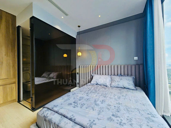 Phòng ngủ chung cư hiện đại với giường đôi ga hoa màu xám cạnh cửa sổ lớn và vách kính nhà tắm