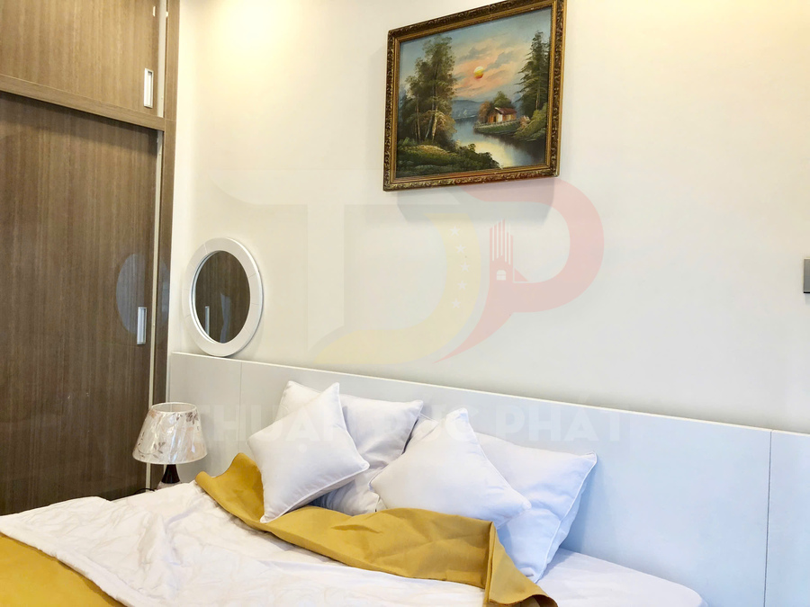 Giường ngủ với chăn ga gối màu trắng vàng, tủ quần áo gỗ và tranh phong cảnh treo tường