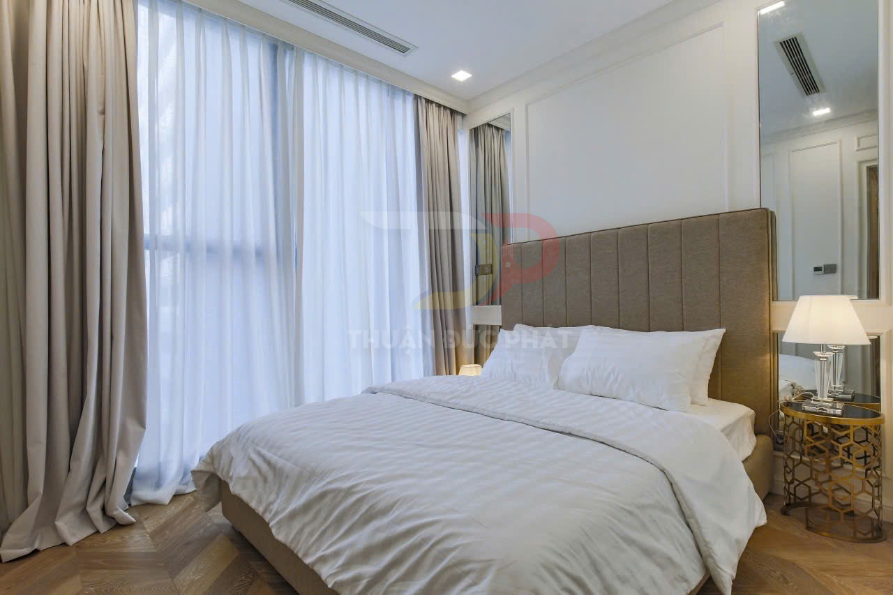 Giường ngủ đôi bọc nệm với ga gối trắng cao cấp trong phòng ngủ hiện đại có rèm cửa lớn và đèn bàn