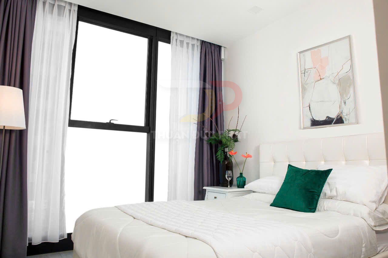Phòng ngủ hiện đại với giường bọc nệm trắng, gối xanh, rèm cửa sổ hai lớp và đèn sàn cạnh giường