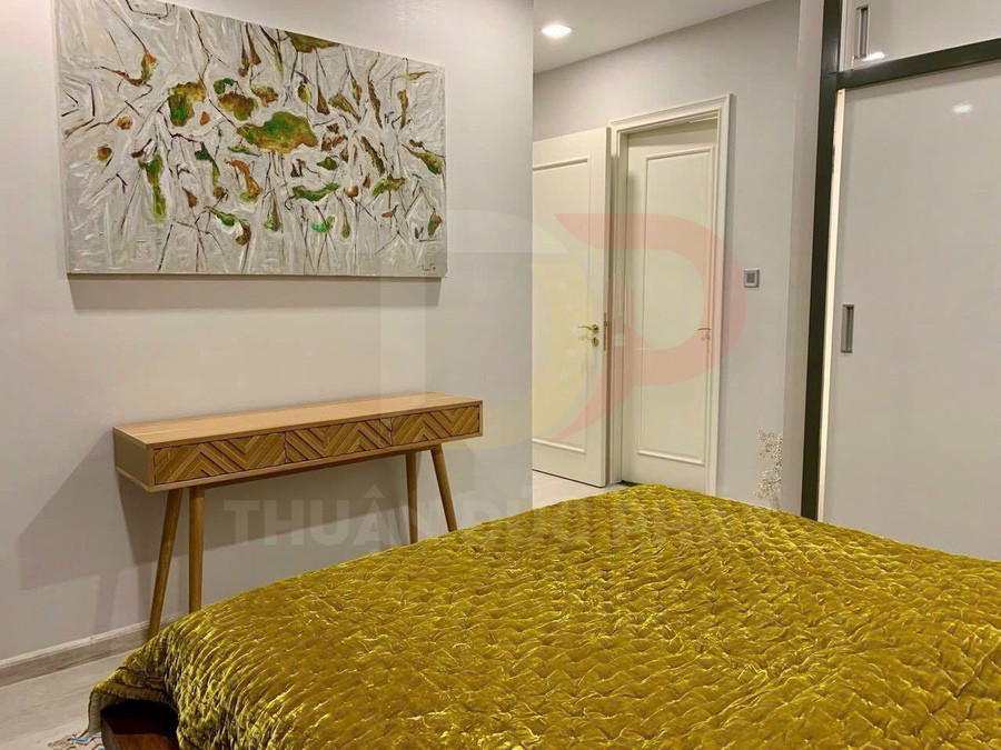 Phòng ngủ hiện đại với giường phủ chăn nhung màu vàng, bàn console gỗ và tranh treo tường trừu tượng