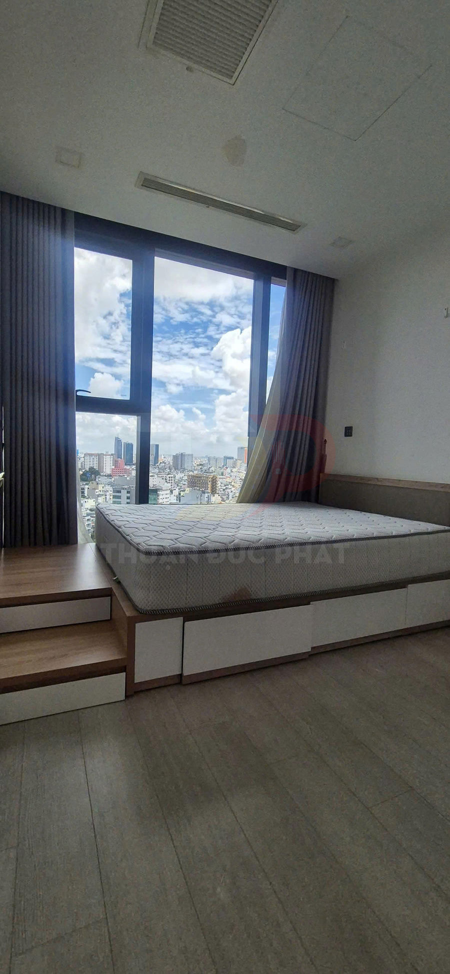 Giường ngủ gỗ có hộc kéo và nệm lò xo cạnh cửa sổ kính lớn view thành phố