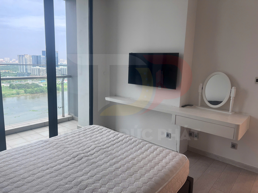 Phòng ngủ chung cư với giường nệm trắng, tivi treo tường và bàn trang điểm cạnh cửa kính view sông