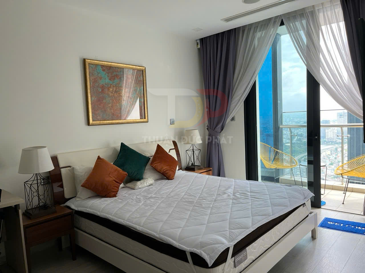 Phòng ngủ chung cư hiện đại với giường nệm trắng, gối trang trí nhiều màu và cửa kính lớn nhìn ra ban công