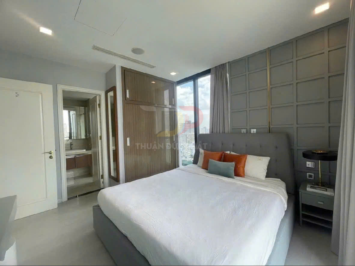 Phòng ngủ hiện đại với giường đôi bọc nệm màu xám, ga trắng, gối trang trí và cửa sổ lớn nhìn ra thành phố
