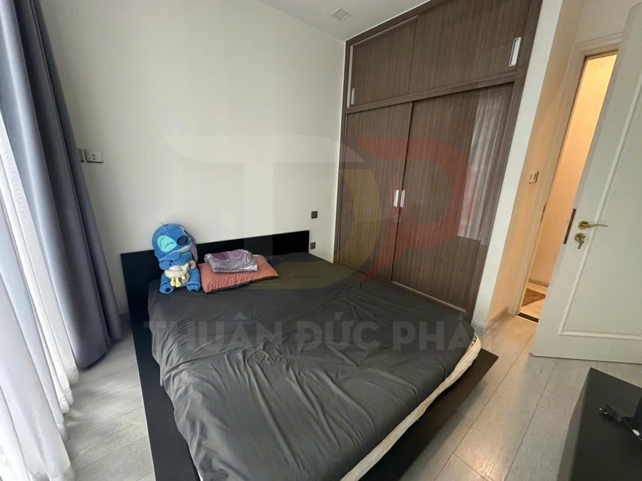 Phòng ngủ nhỏ với giường nệm màu xám, tủ quần áo gỗ âm tường và rèm cửa sổ sáng màu