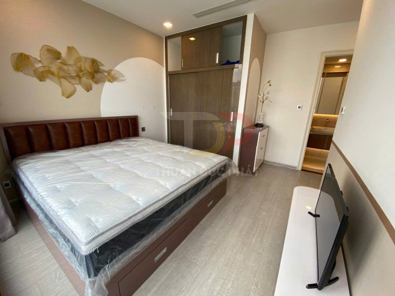 Phòng ngủ hiện đại với giường nệm lớn, tủ quần áo gỗ âm tường và tivi đặt trên kệ đối diện giường