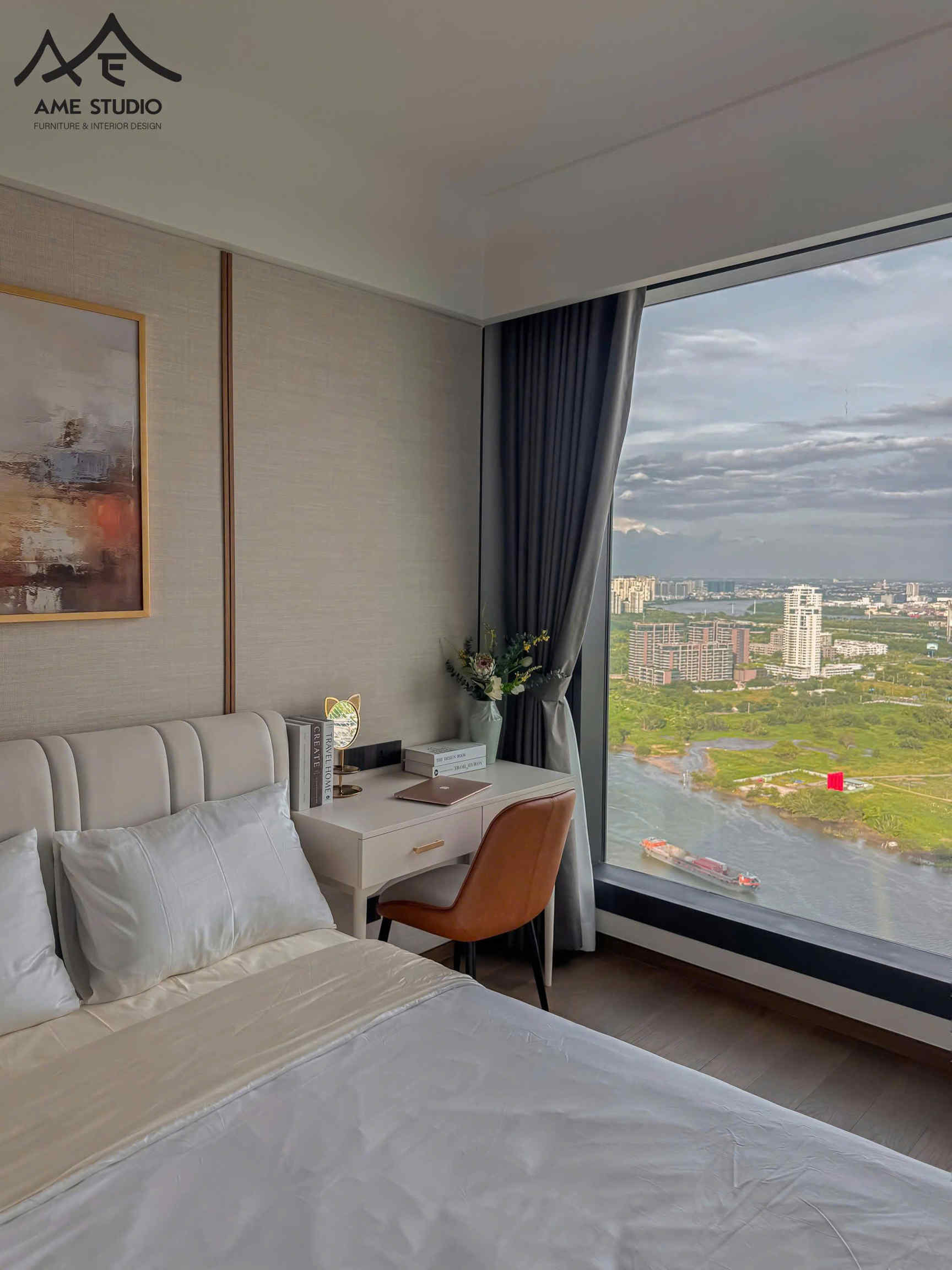 Phòng ngủ hiện đại với giường bọc da, bàn làm việc cạnh cửa sổ lớn view sông và thành phố